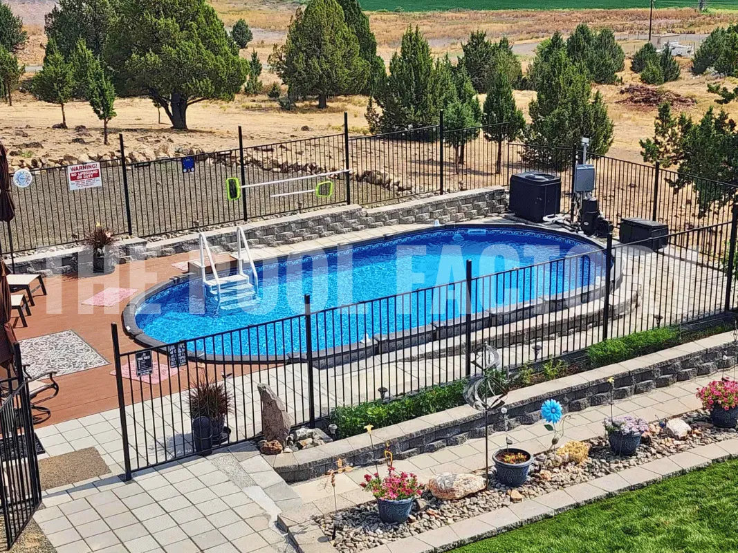Oval semi-inground backyard pool with stone pathway, trimmed grass, and vibrant landscaping on a sunny day