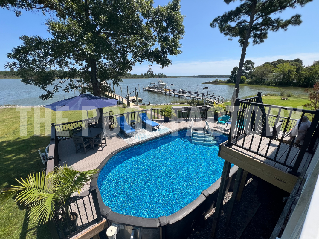 Semi-inground oval saltwater pool with lights, greenery and a lake view