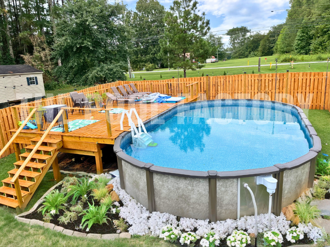 Oval pool with partial deck, flowers, shrubs and greenery