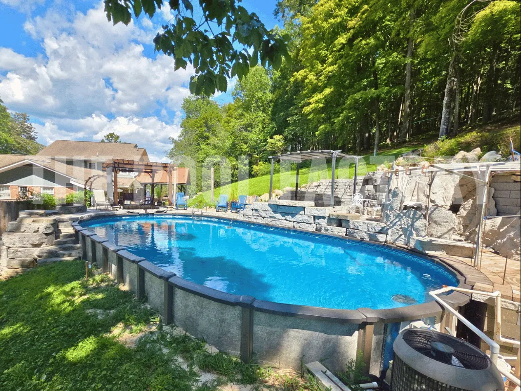 Luxury oval saltwater pool with stone landscaping and outdoor seating beside woody tree line