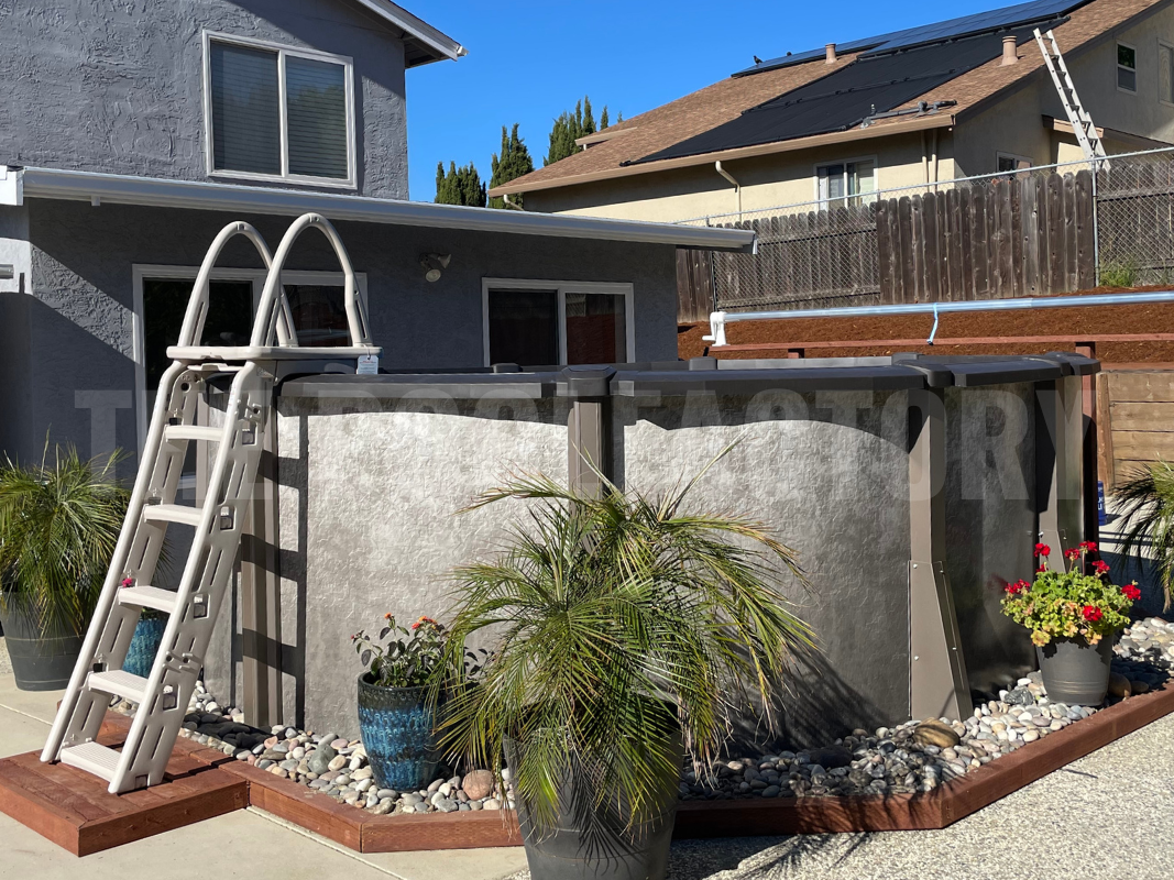 Above ground oval swimming pool on cement with a sandbox covered with landscaping rocks
