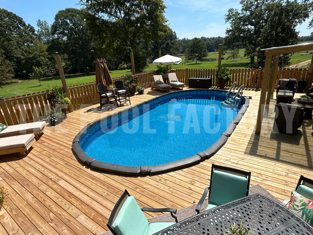 Oval above ground swimming pool with full wrap around deck and bright sunny landscaping surrounding