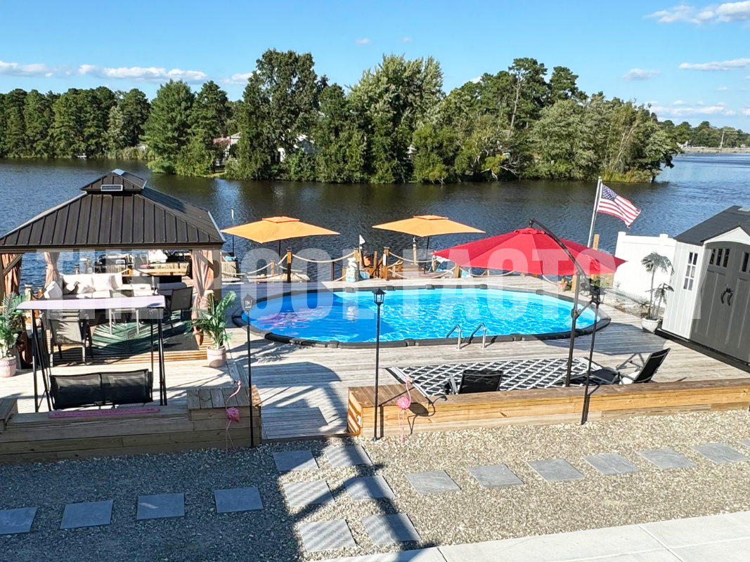 Semi-inground oval swimming pool with full deck, gazebo, lounge seating with a stunning lake view