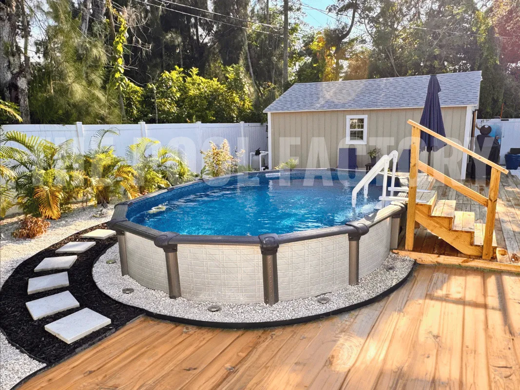 Backyard semi-inground pool surrounded by stone walkway, wood patio, and tropical plants