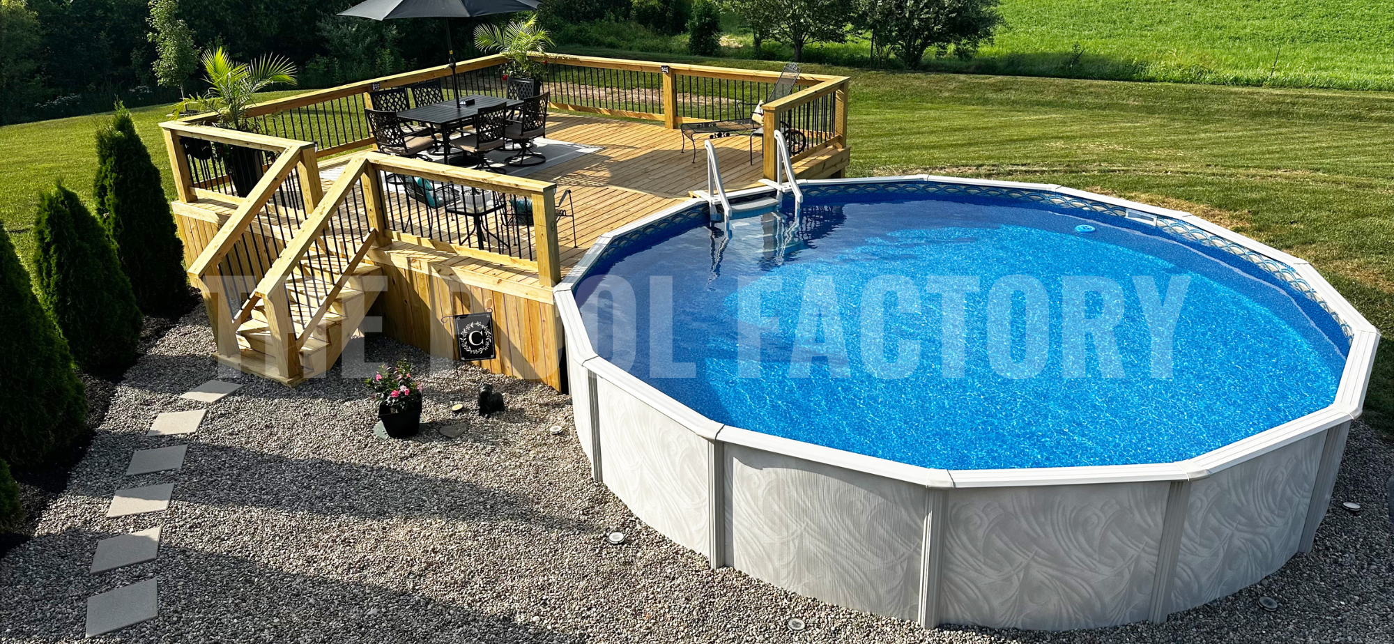 Backyard with a round above ground swimming pool with lush landscaping, partial deck and large shrubs surrounding