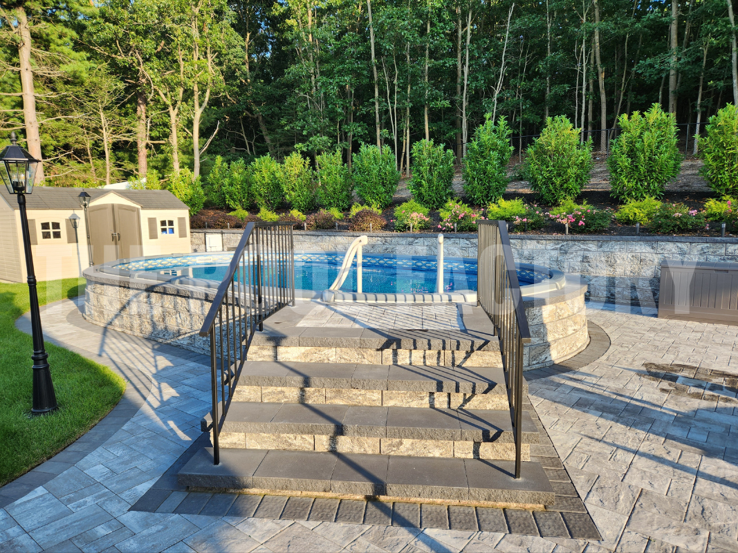 Oval semi-inground pool with stone patio on a sunny day