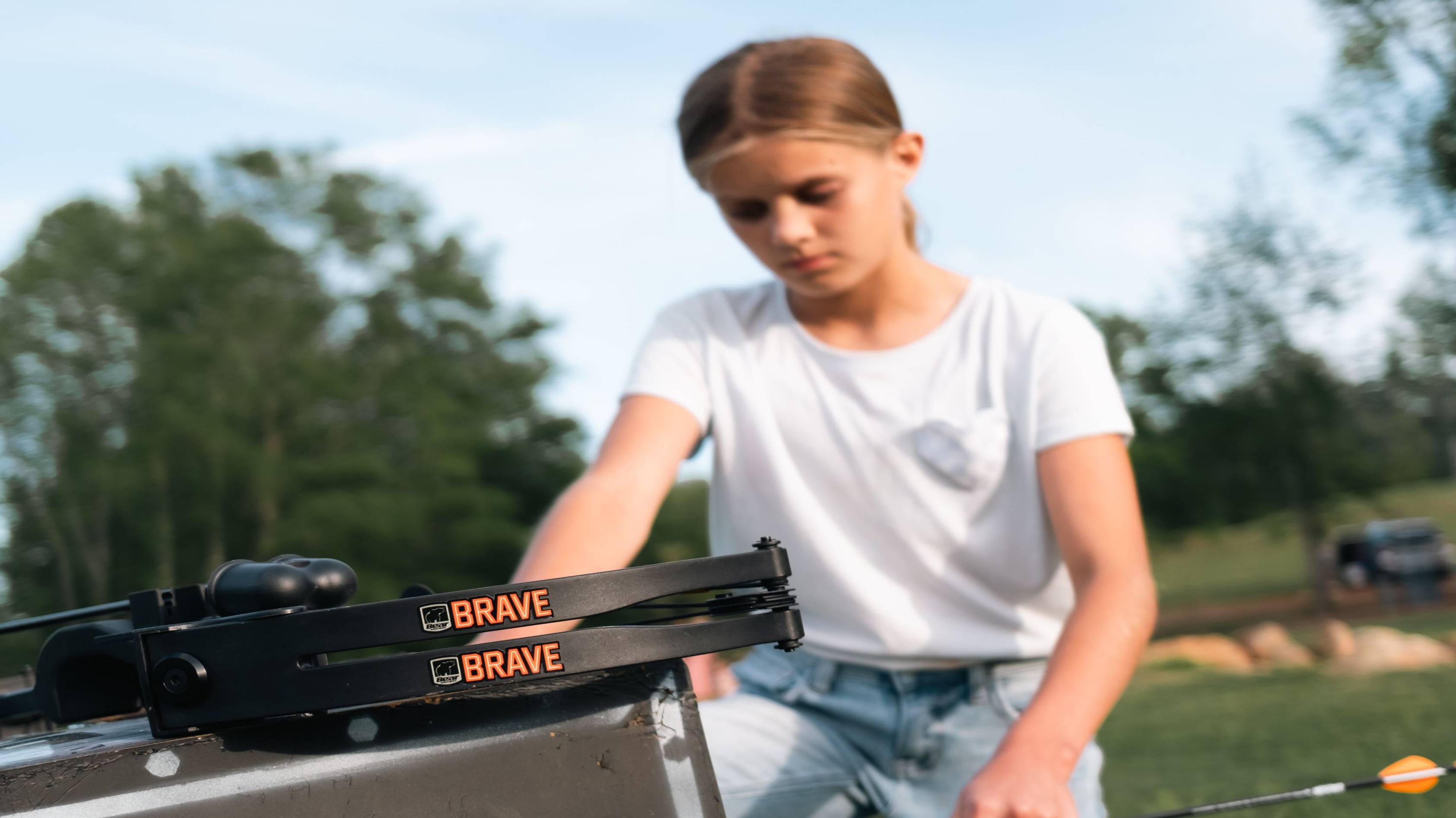 A close up of the Bear Archery Brave youth bow in front of a girl pulling arrows out of a target