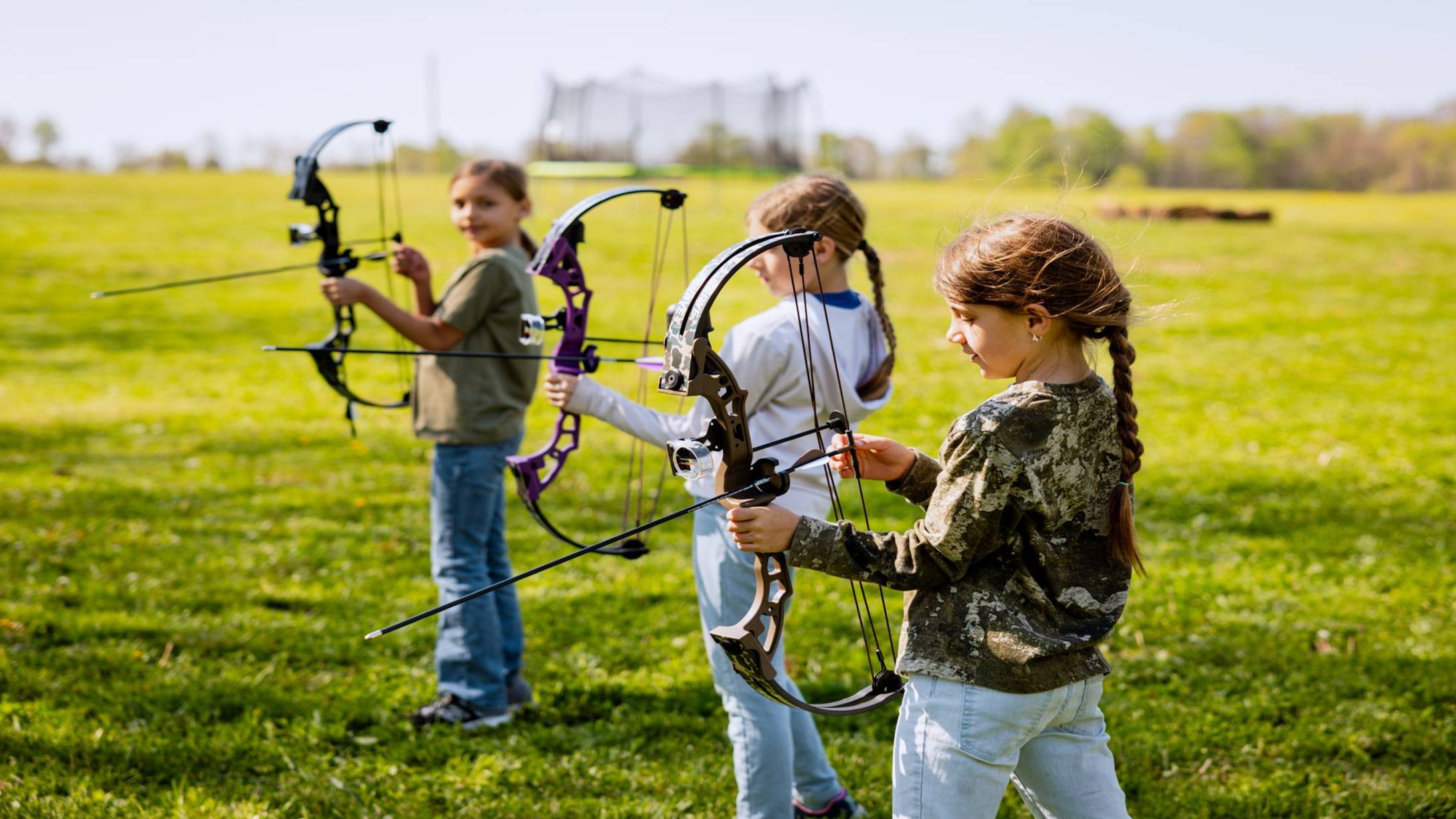 Three girls preparing to shoot the Brave youth bow from Bear Archery.