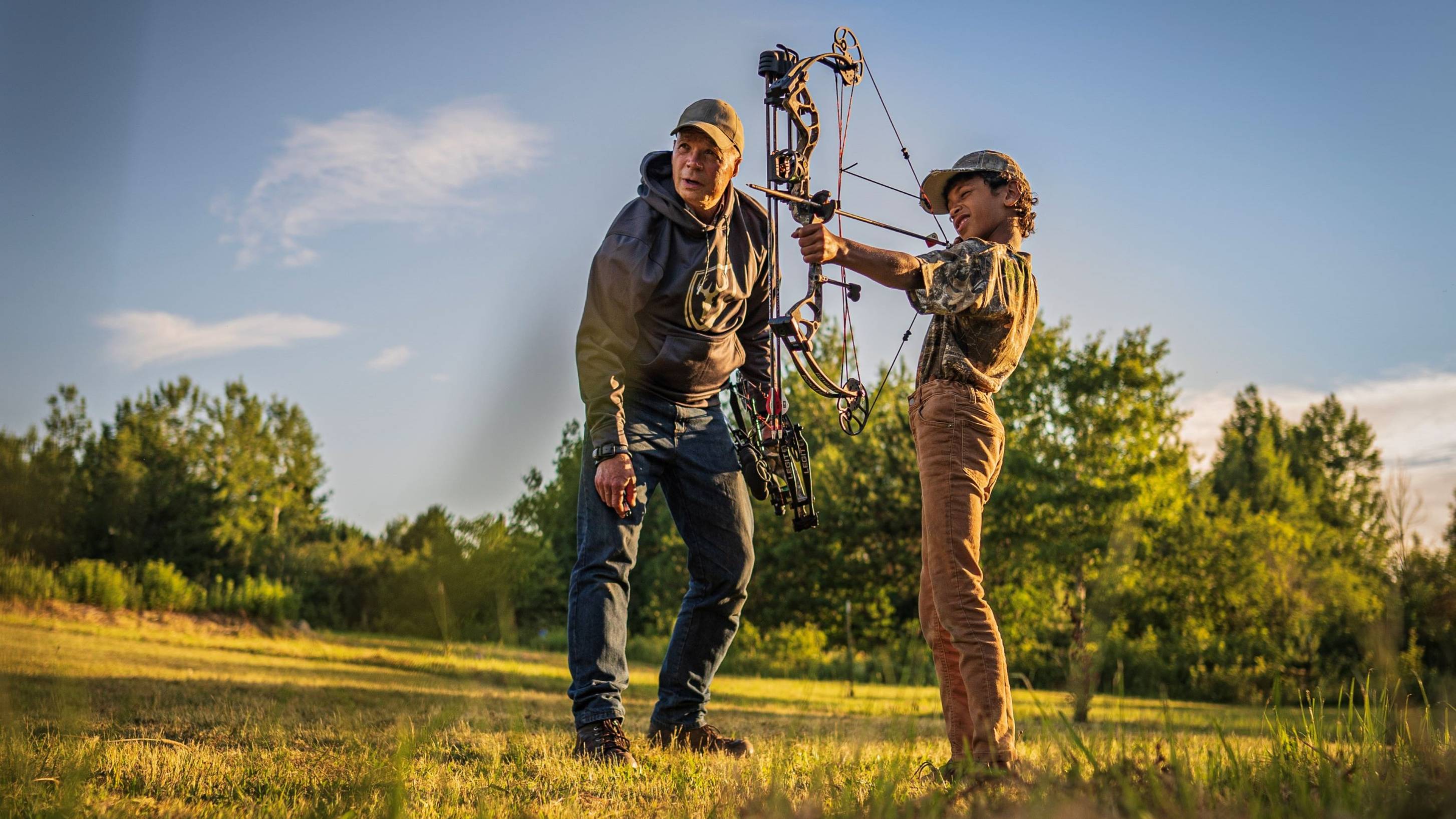 Father helping son in a field shooting the Bear Archery Royale youth compound bow. 