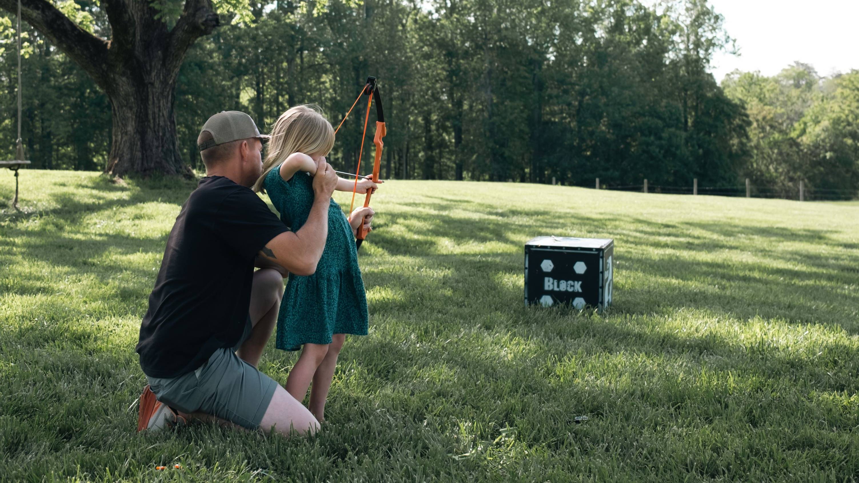 Dad helping daughter shoot the Apprentice youth bow from Bear Archery at a target in a field
