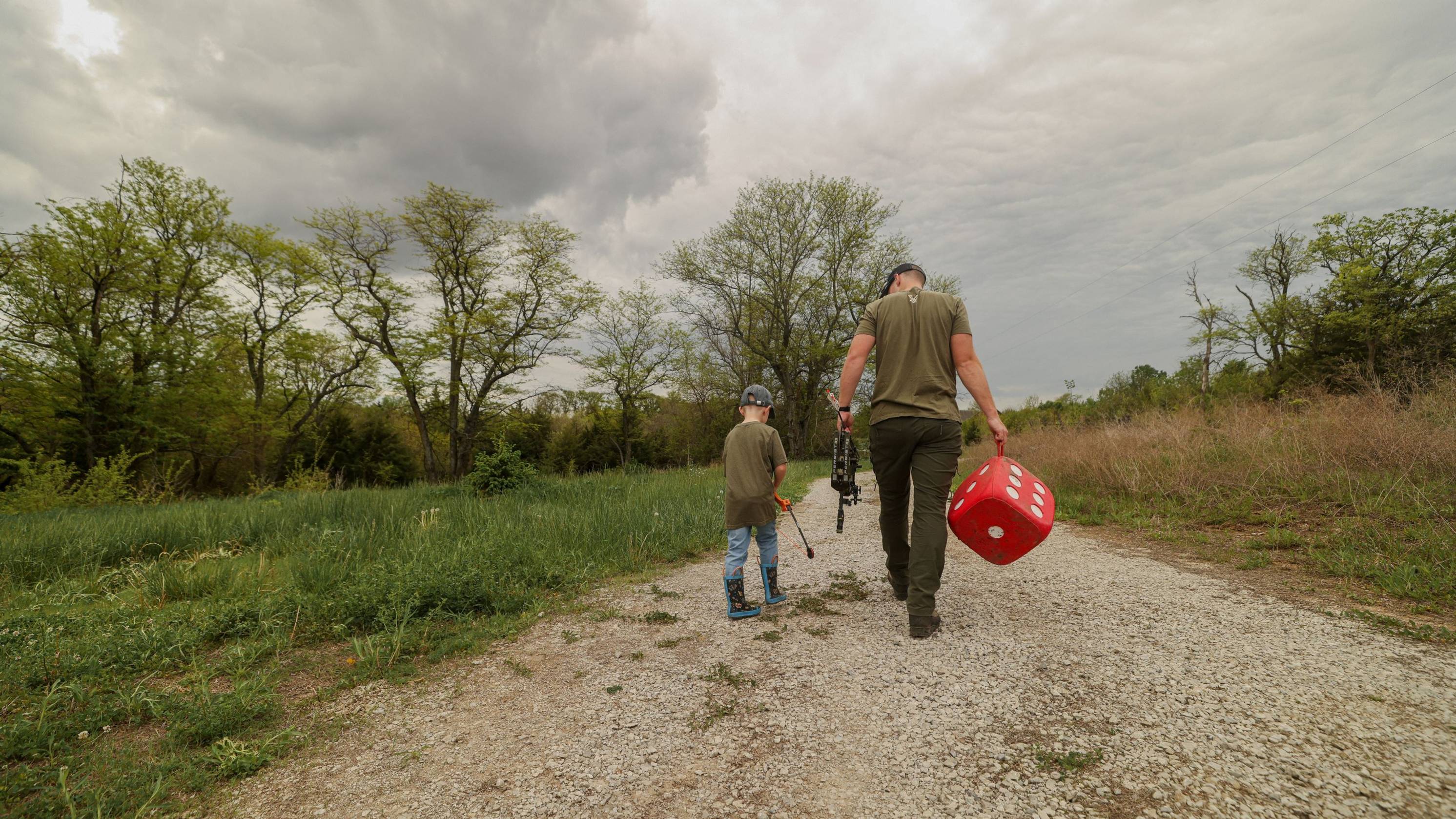 Father and son walking with the Bear Archery Spark youth bow, the Persist 33 compound bow, and an archery target