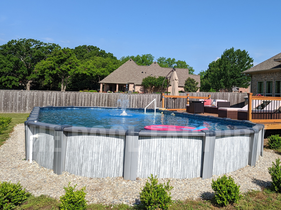 Oval above ground pool with trees, shrubs, and decorative stones