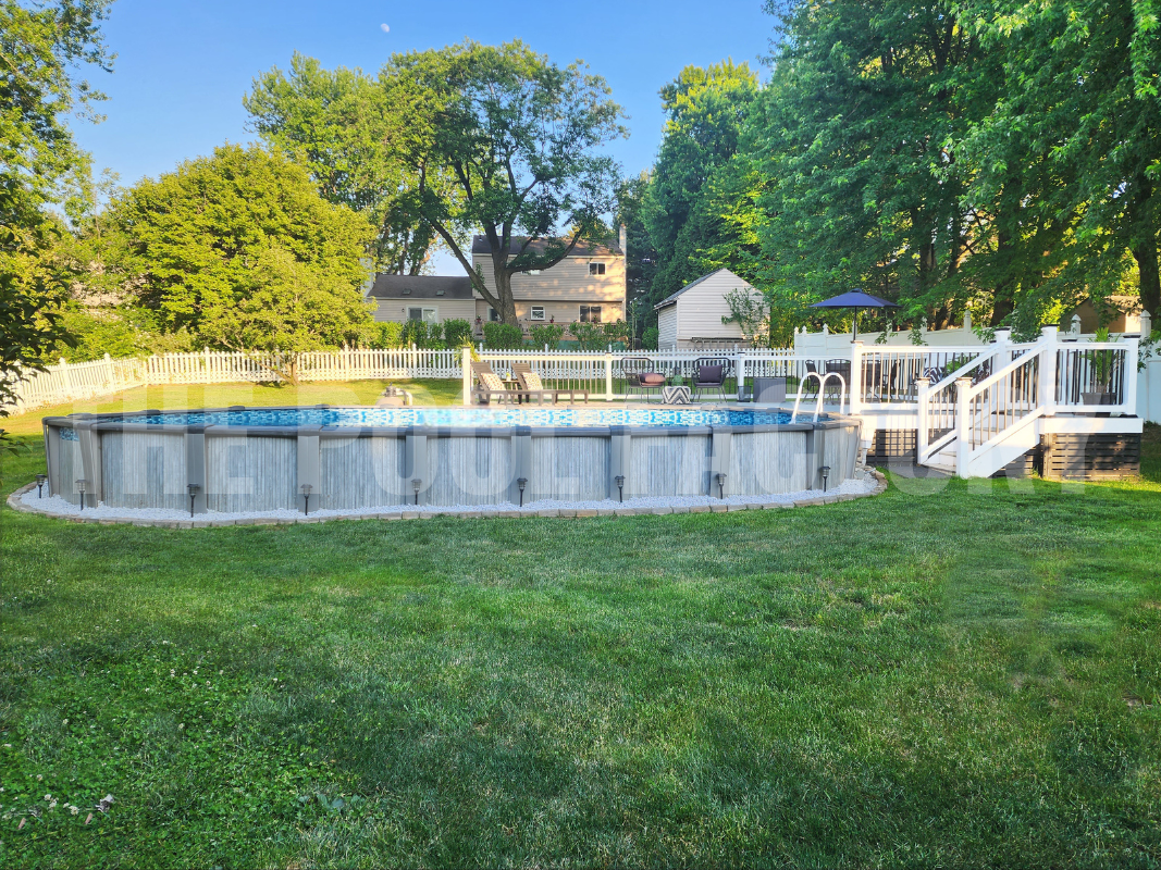 Oval above ground pool with sunlit landscaping and a wooden deck