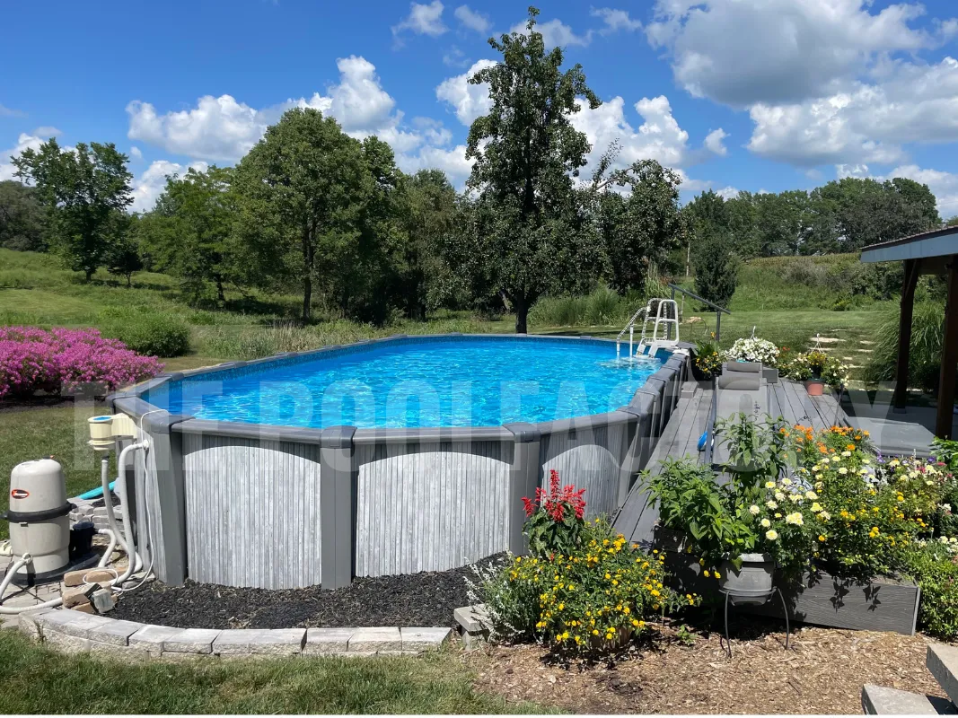 Oval above ground pool surrounded by lush flowers, vibrant landscape, and a scenic tree line in the background