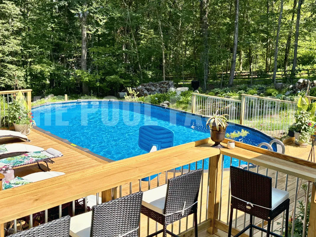Oval backyard pool with wood deck, rattan lounge chairs, and landscaped backyard