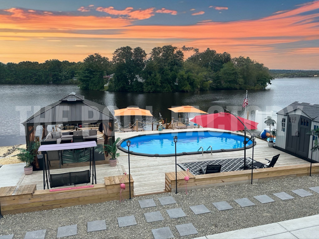 Semi-inground salt water oval swimming pool with full deck, gazebo, lounge seating with a stunning sunset lake view