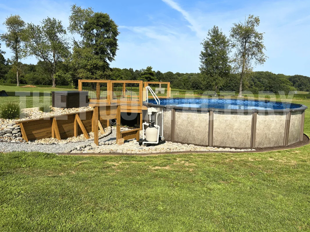 Round above ground pool with mulch bed, green grass, and partial deck on one side