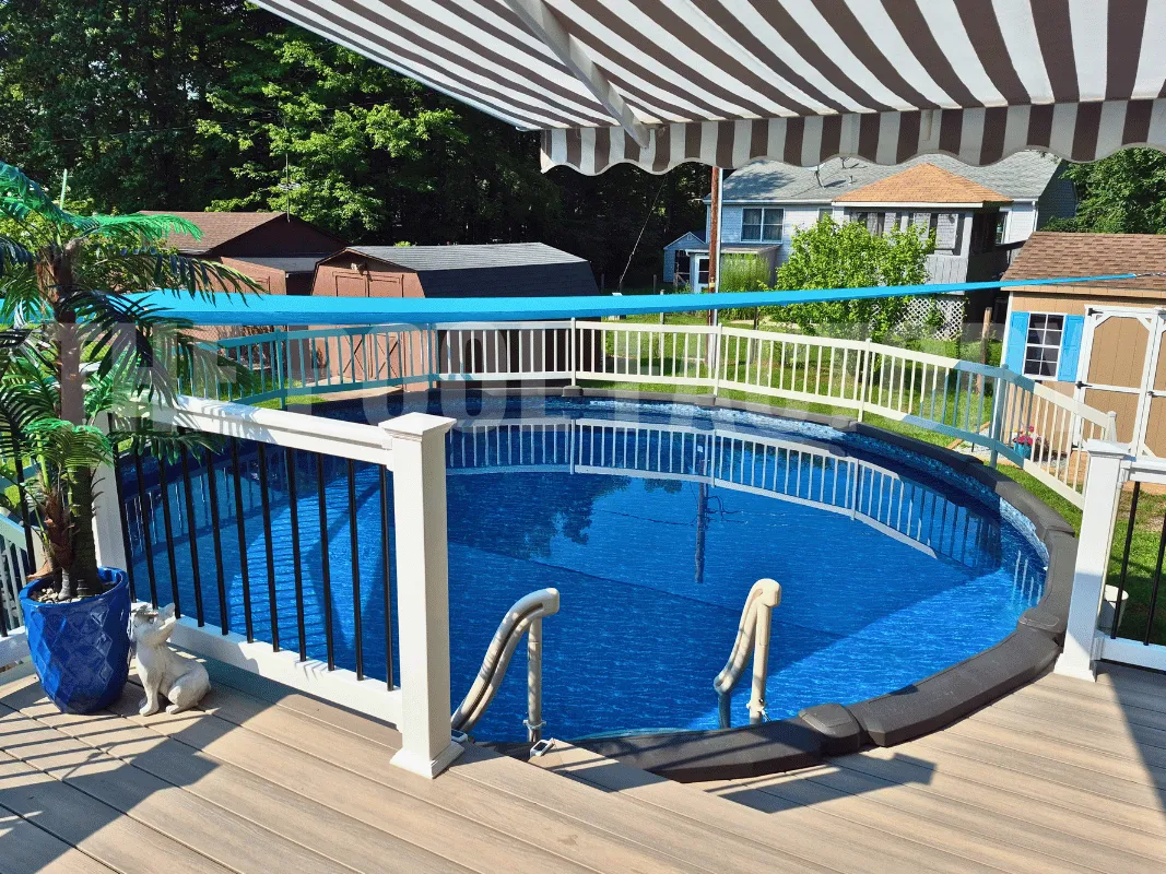 Round backyard pool with partial deck, flower planters, and awning for shade
