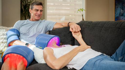Man and women on the couch using their Celluma devices over the knees, elbow and face and an aging and pain treatment using blue, red and near-infrared light therapy.