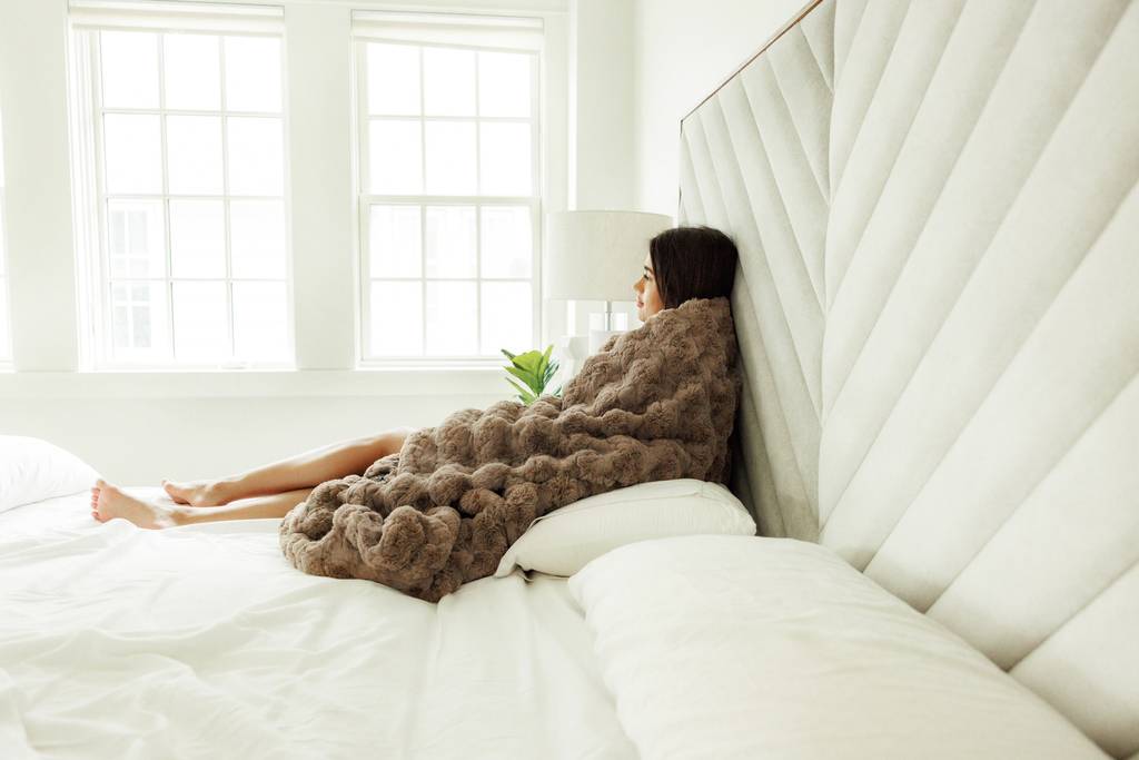 Woman holding a soft weighted blanket on a bed after proper washing and drying