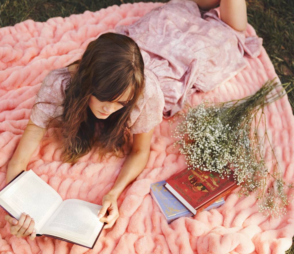 Woman relaxing with soft spring bedding ideas and layered pink textures in a cozy bedroom