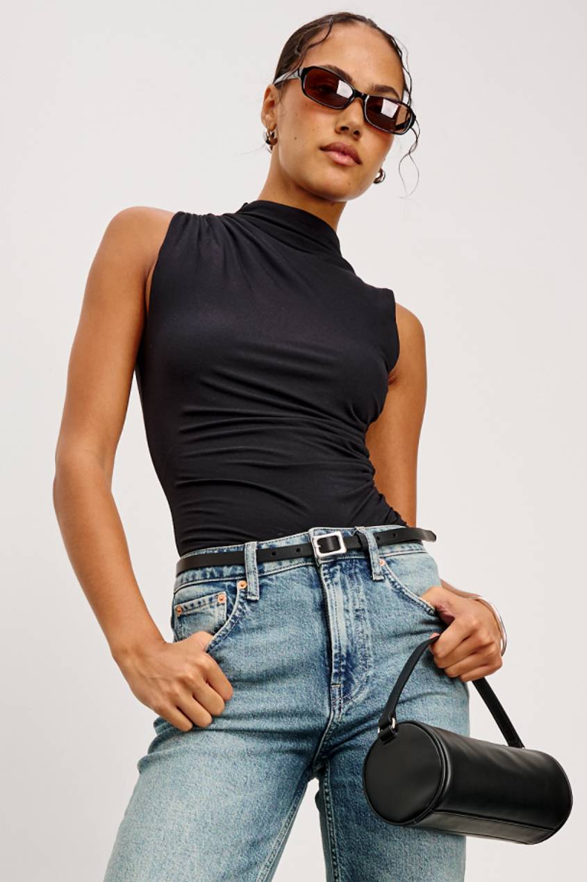 Woman wearing a black sleeveless top and light-wash jeans, carrying a black structured shoulder bag.
