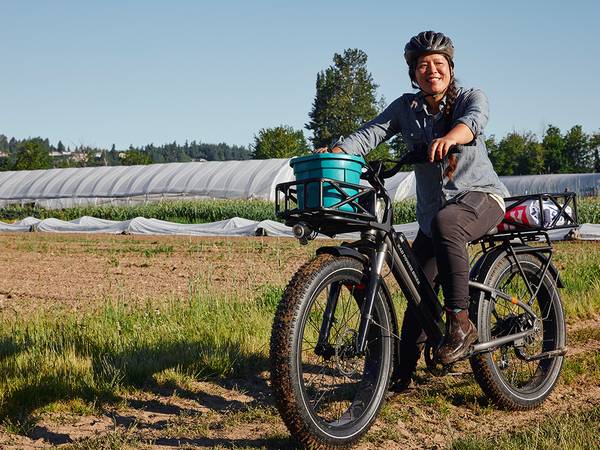 A woman rides a RadRover 6 Plus loaded with farming equipment in front of a farm
