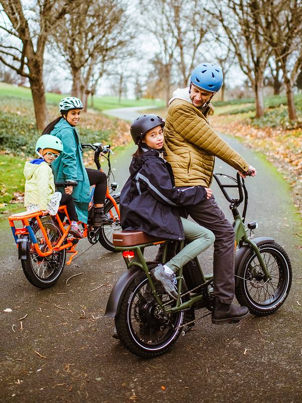 A man with a child on the rear of a RadRunner 2 ebike and a woman with a child on the rear of a RadWagon cargo ebike
