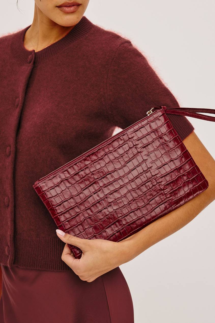 Woman wearing a burgundy cardigan and carrying a burgundy croc-effect clutch.