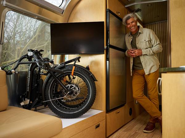 A man relaxes in an RV next to a folded black RadExpand ebike