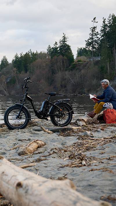 Man sitting on a beach next to an electric folding bike