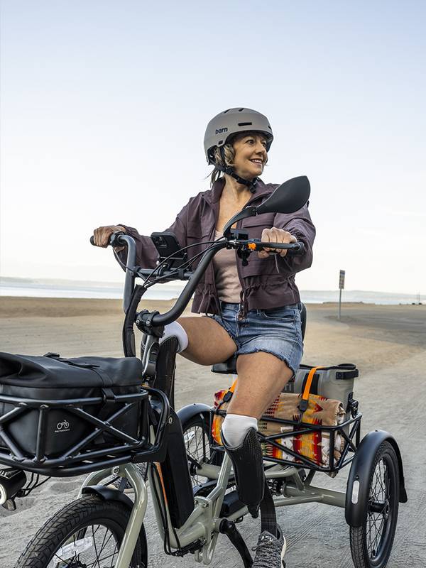 Woman with prosthetic legs riding an electric tricycle near the beach