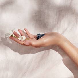 An open hand holds small flowers with blueberries against a Blush Linen Flat Sheet backdrop. 
