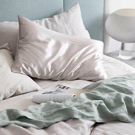 Bed styled with the Smoke Gray Duvet Cover set, a Smoke Gray Fitted Sheet, Sage Flat Sheet with Border and a Smoke Gray Silk Linen Flip Pillowcase. Also featured is an open magazine positioned atop the sheets.				