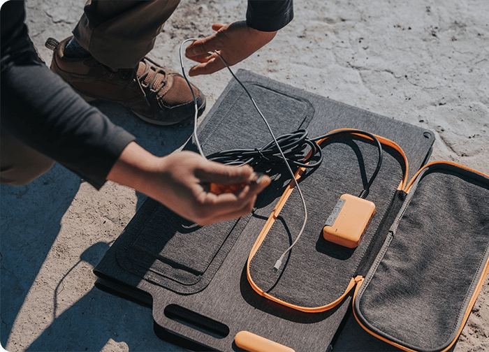 A person is organizing charging cables and a power bank on a flat, textured surface.