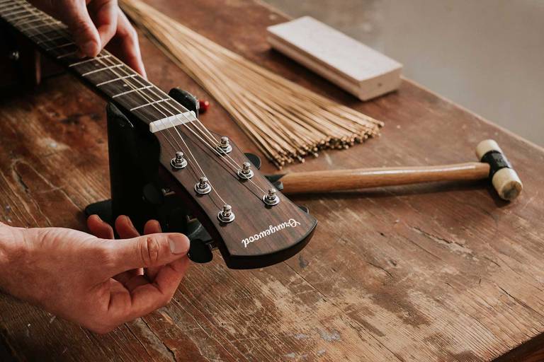 Guitar tech setting up an Orangewood guitar on a workbench with extra strings in the background.