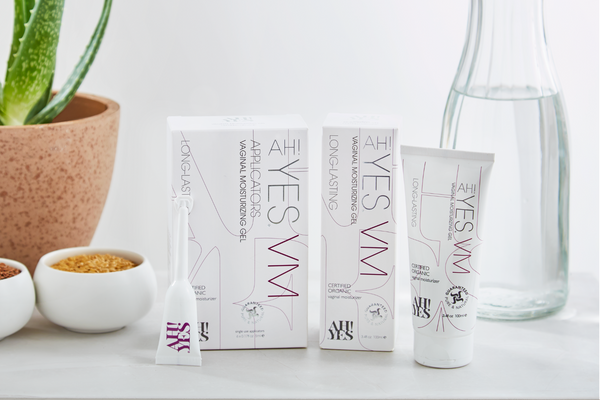 AH! YES VM range including a vaginal moisturizer tube and an applicator next to their boxes. In the background is an aloe plant and a jug of water
