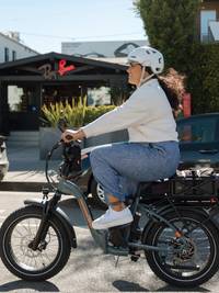 Image of a woman riding the RadExpand 5 Plus ebike in Slate Blue. The bike is showing an assortment of accessories including the large basket, large roll-top liner and handlebar bag. 
