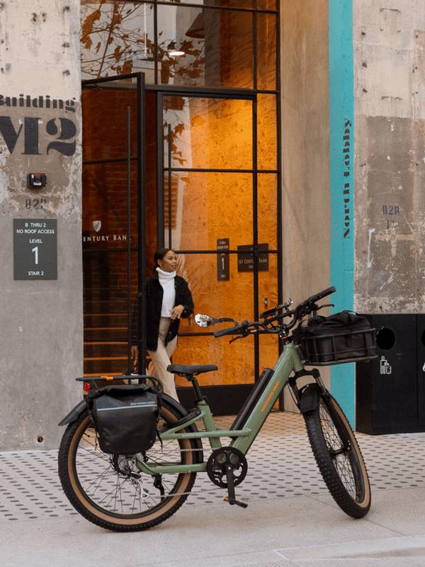 Green Radster Trail electric off-road bike parked in front of a building, with a woman walking through the entrance.