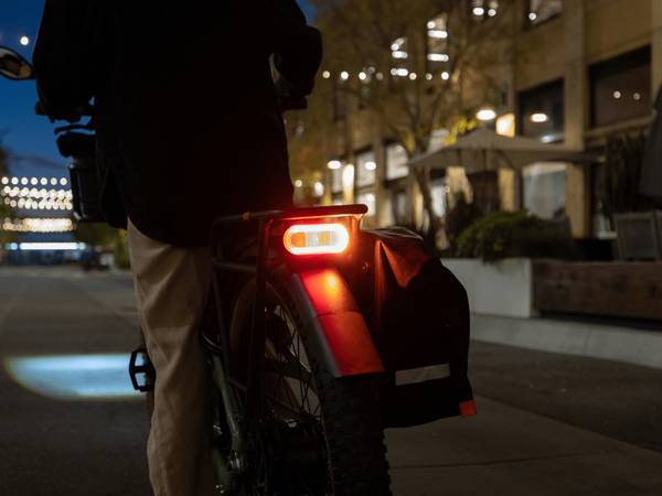 Person standing by a Radster Trail electric off-road bike in the dark, with the rear light lit