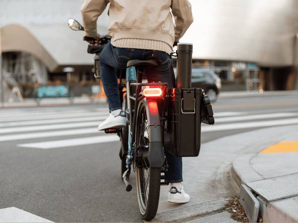 Person on a Radster Road electric commuter bike, stopped at a corner showing the brake light in use. 