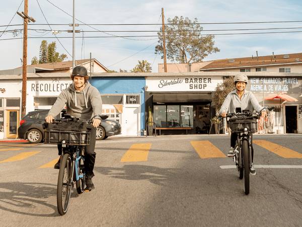 Two people riding ebikes on a street, both on a Radster Road electric commuter bike with baskets and other accessories. 
