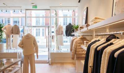 Bright and airy Sloane Street store interior with racks of neutral-toned clothing, mannequins dressed in elegant outfits near the entrance, and large front windows letting in natural light