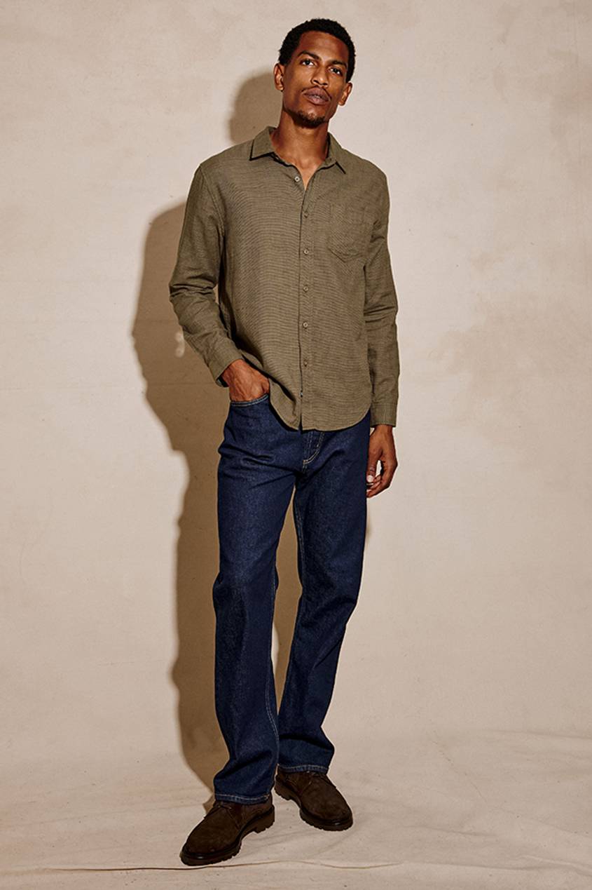 Link to Shop Men's New Arrivals at Rails. Image shows a man standing infront of a plain background, wearing a dark green button down shirt and dark jeans from the Men's Fall Collection.