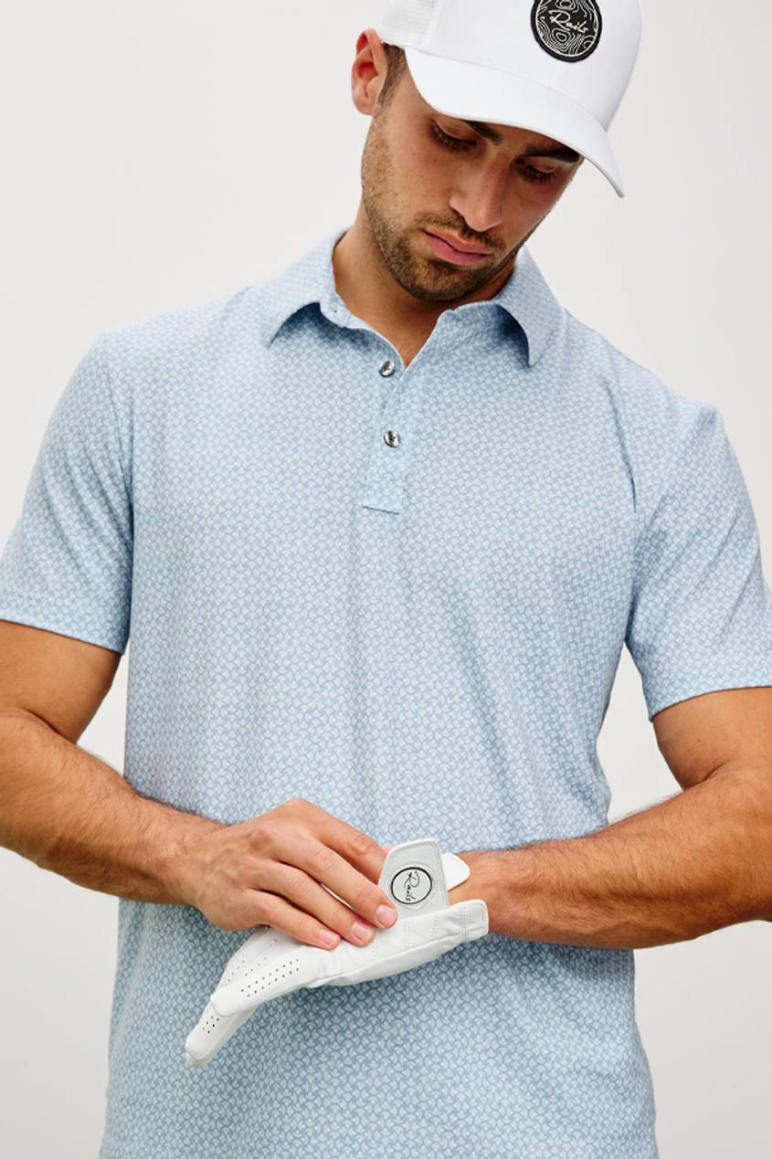 A man fixing his white golf glove while wearing a blue golf polo and white golf hat.