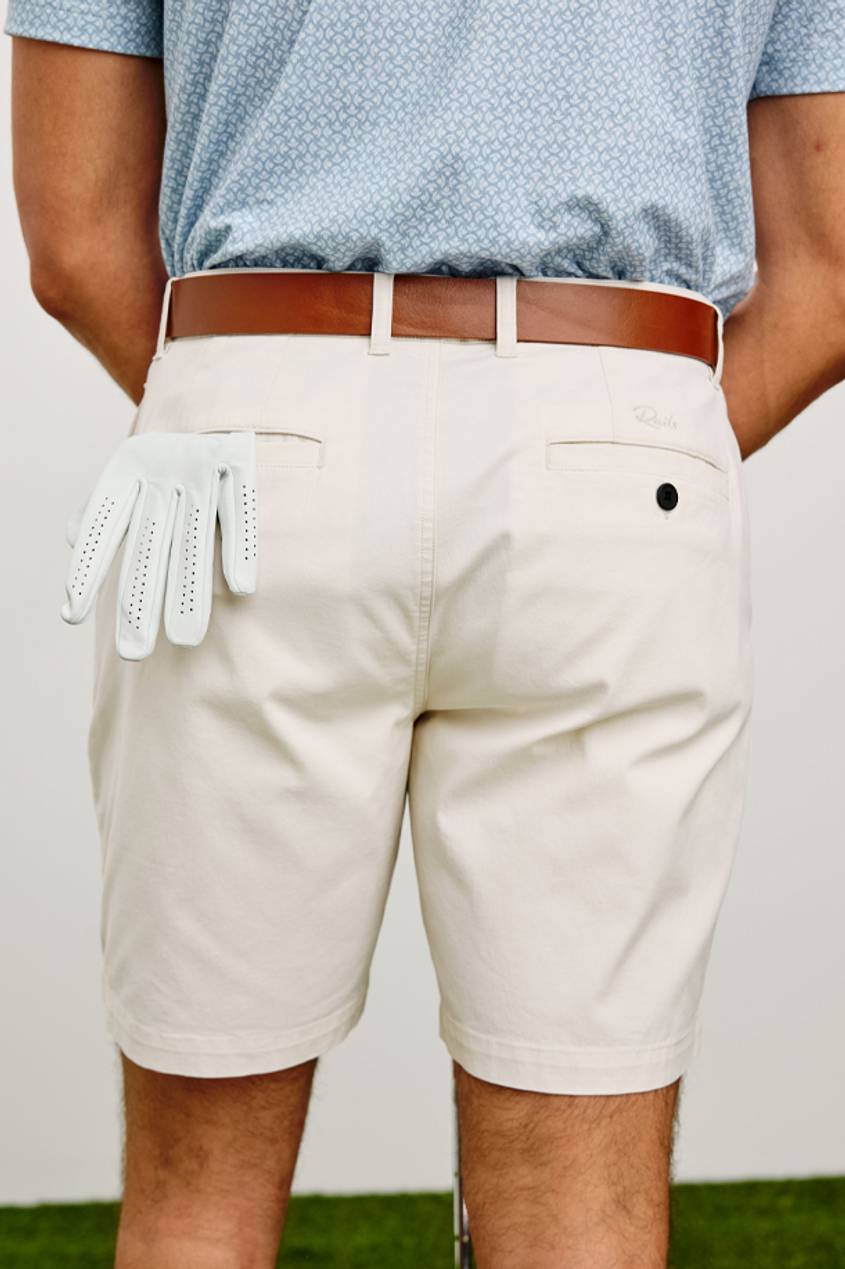 A back view shot of a man wearing beige golf shorts, a brown belt, and a white golf glove hanging outside of his back left pocket.