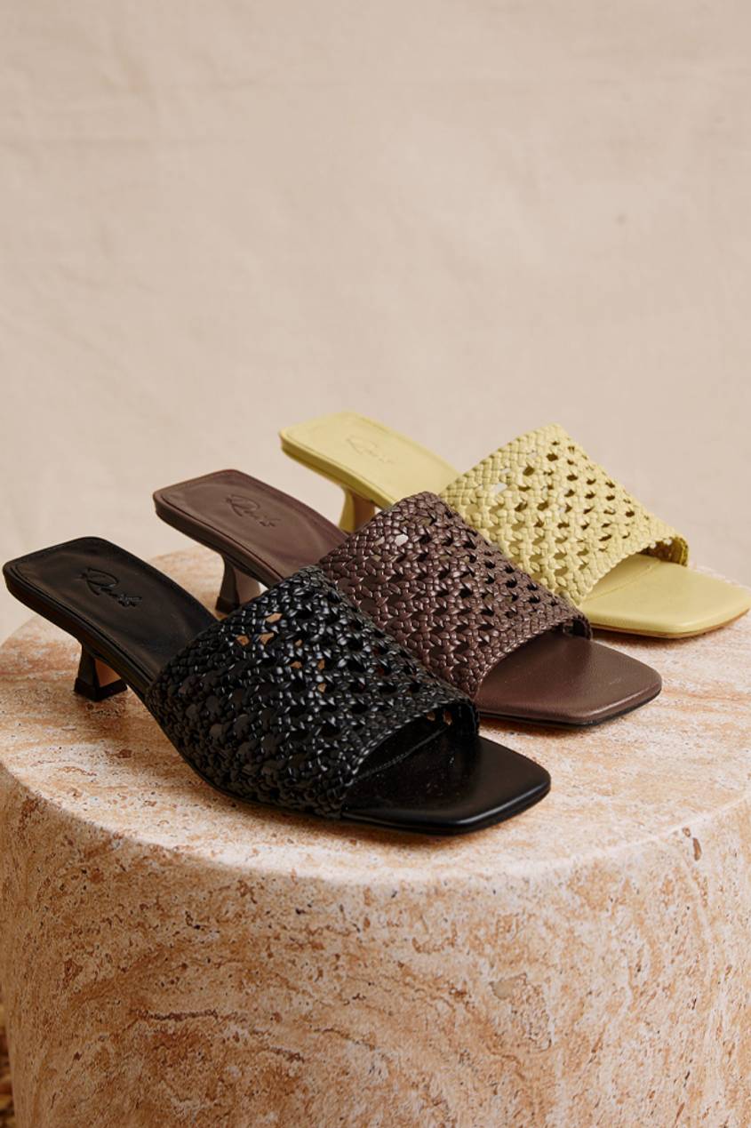 A black, brown, and yellow pair of different colored woven heels displayed on a marble textured surface.