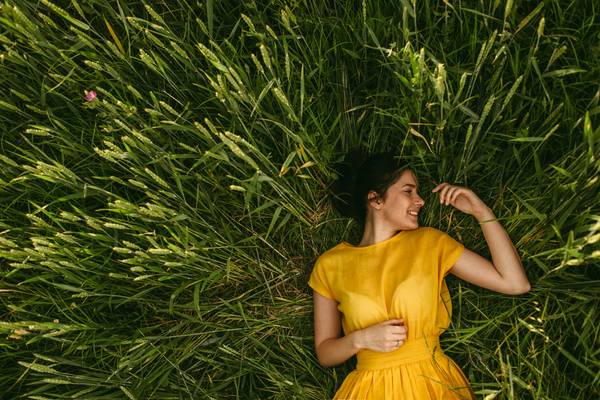 Woman laid in long green grass, wearing a yellow dress