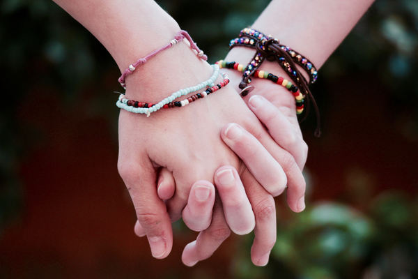 Two holding hands, several friendship bracelets in each wrist against a dark background