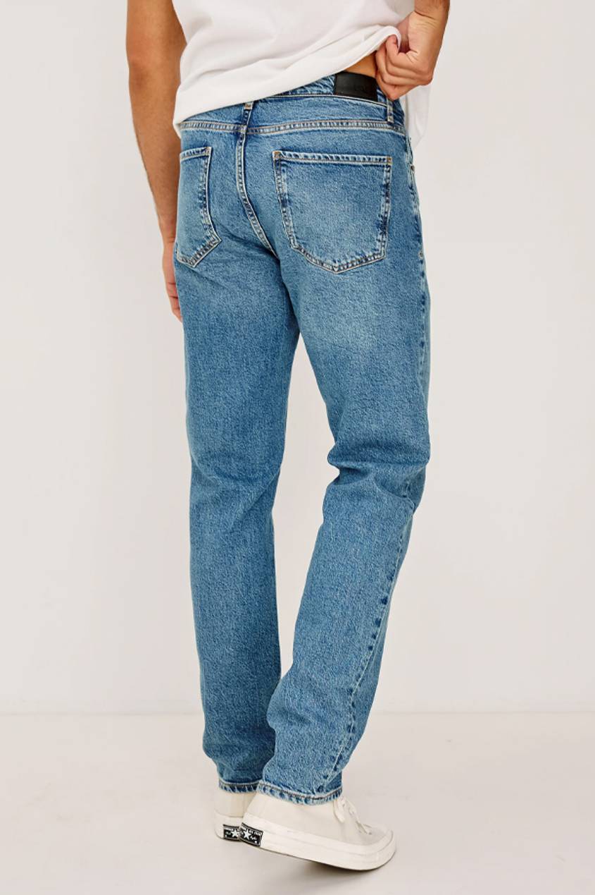 Back view of a man wearing a pair of clayton slim straight jeans in a medium blue wash.